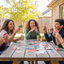 Group of friends playing card games outdoors at a wooden table.