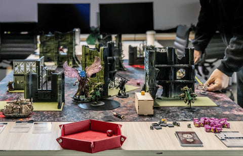 Tabletop wargame setup with painted miniatures, dice, cards, and terrain pieces.