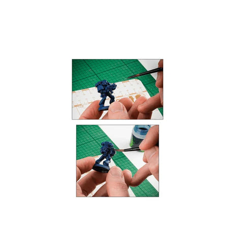 Hand painting a blue miniature figure with a fine brush on a hobby cutting mat