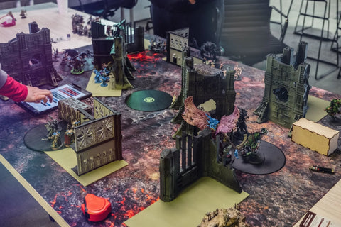 Tabletop miniature wargame with painted figures, terrain, and players in action