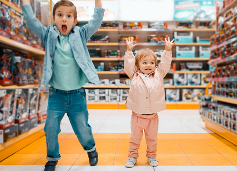 Two children with arms raised in a toy store aisle.