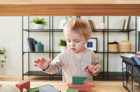 Child playing with wooden blocks in a room with shelves and plants