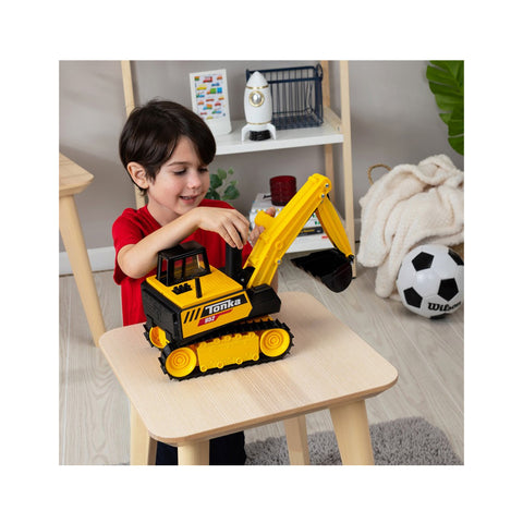 Child playing with yellow toy excavator on small table in playroom with soccer ball