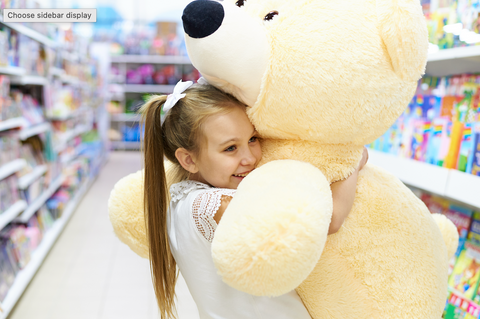 Child hugging a large teddy bear in a store aisle