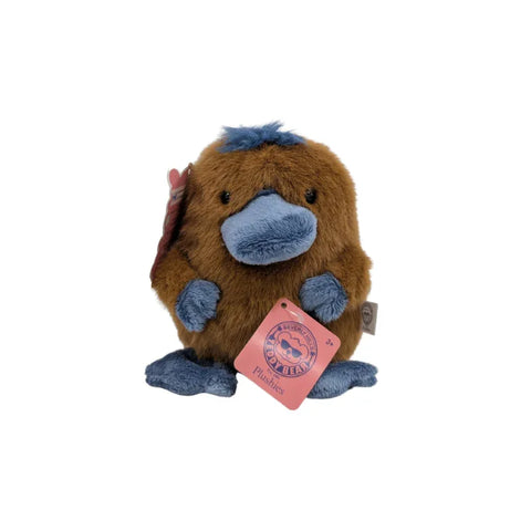 Plush platypus toy with brown fur and blue bill, feet and tag, isolated on white background
