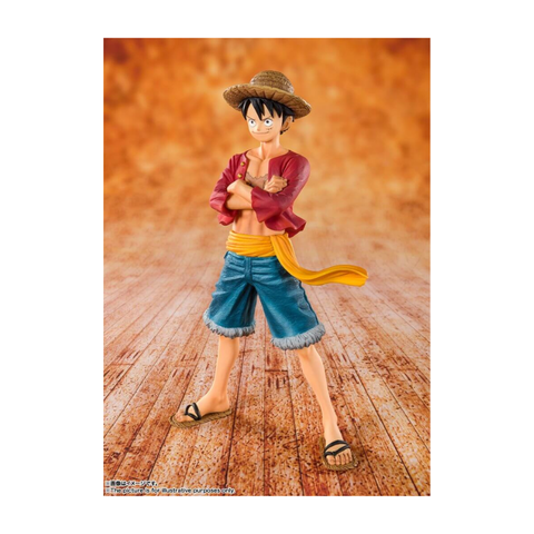 Anime action figure with straw hat, red jacket, and blue shorts on wood floor background.