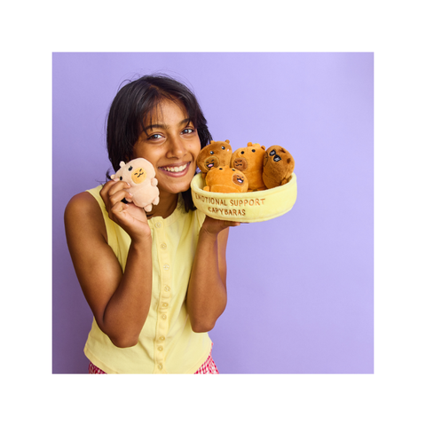 Woman holding cute capybara plush toys in a yellow bowl against a purple background