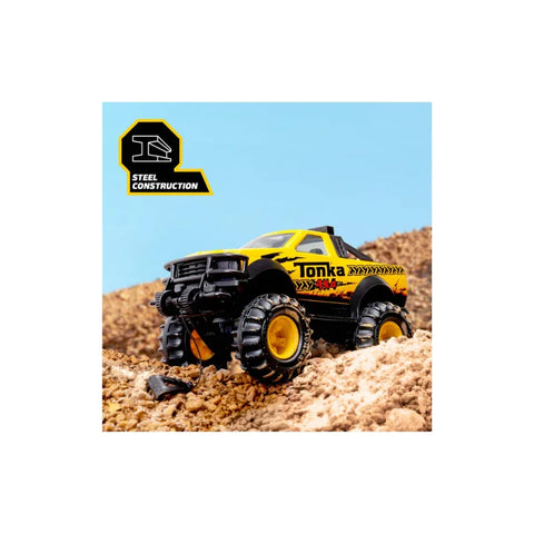 Yellow toy monster truck with steel construction driving on rocky dirt terrain, blue sky background.