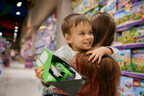 Child holding a toy car in a toy store with a woman behind them