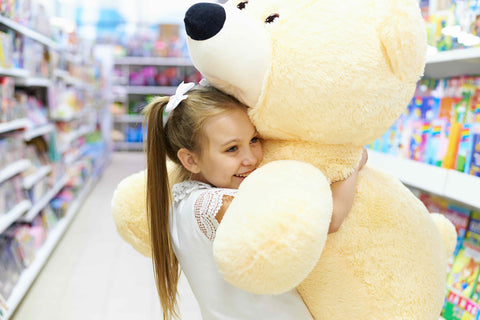 Child holding a large teddy bear in a toy store aisle