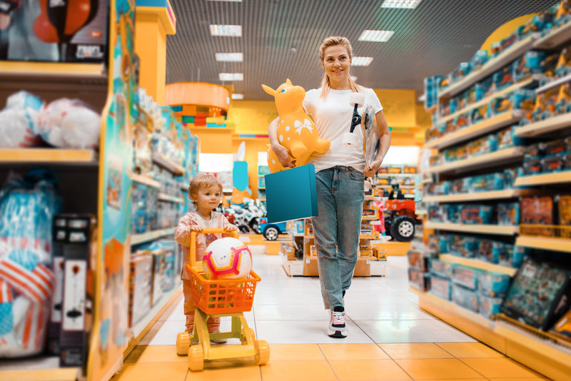 Woman and child in a toy store with shelves of toys and a shopping cart.